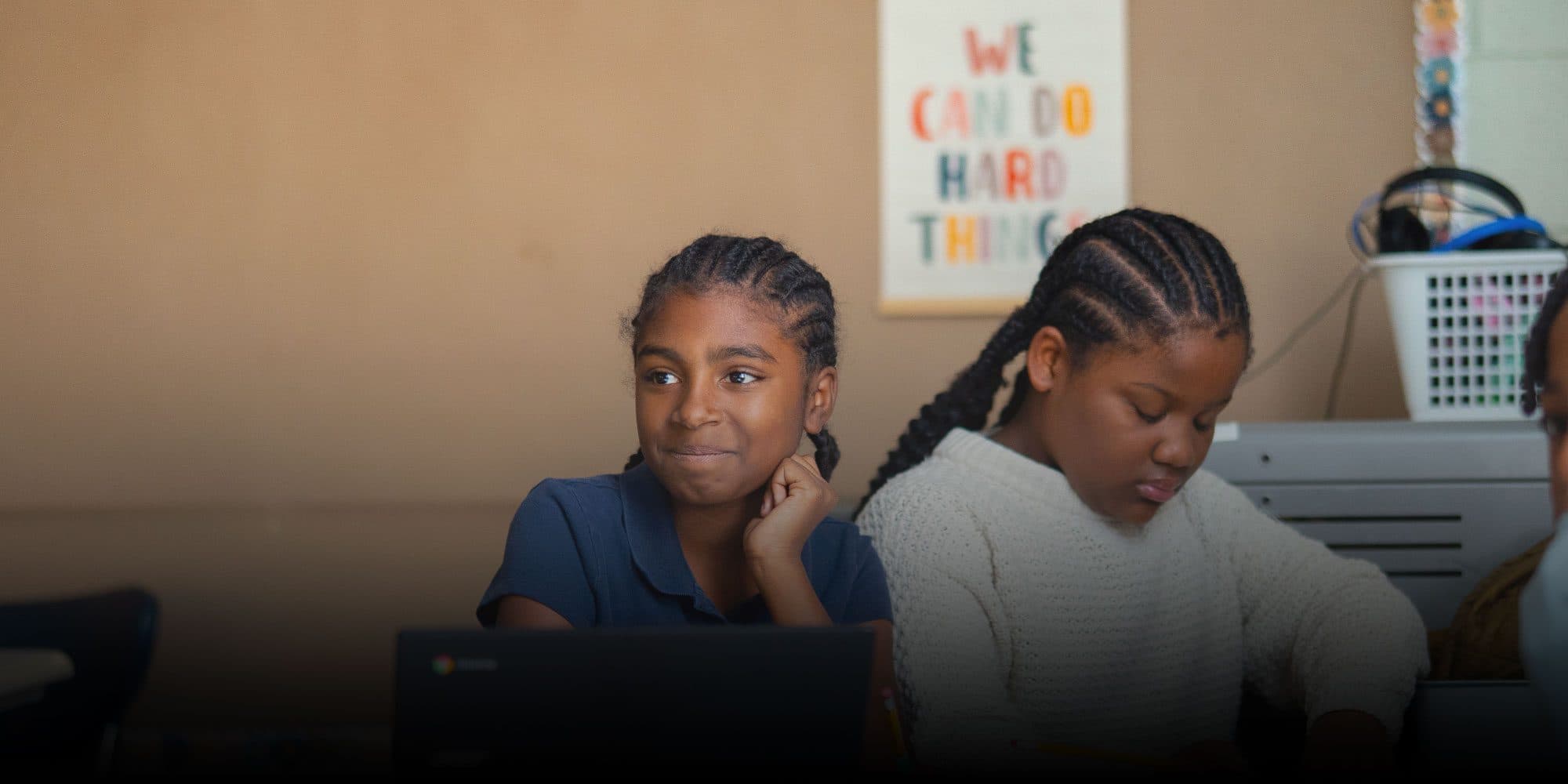 Two students working in a classroom under a "We Can Do Hard Things" poster.